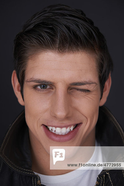 Junger Mann mit strahlend weißen Zähnen zwinkert  Porträt