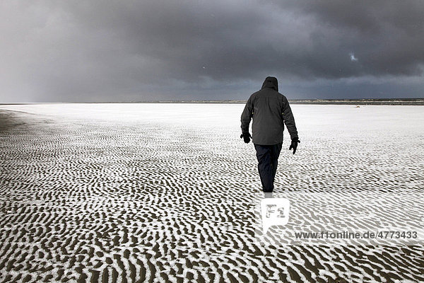 Person walking along the snow-covered beach on the East Frisian North Sea island of Spiekeroog  Lower Saxony  Germany  Europe
