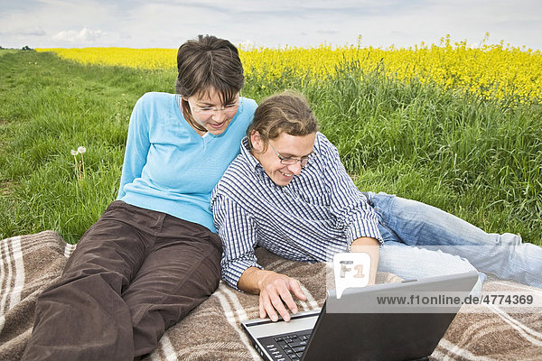 Young couple in front of a laptop in a meadow near a canola field