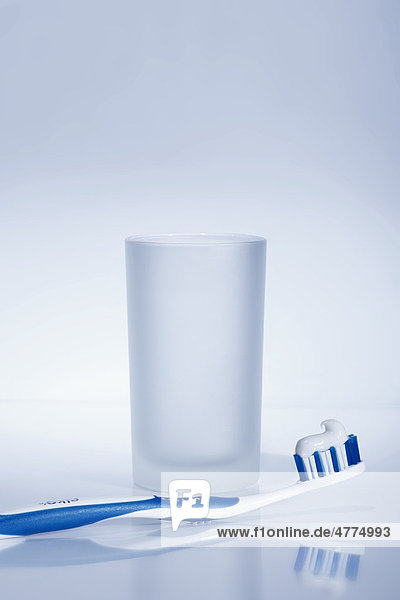 Blau weiße Zahnbürste mit Zahnpasta und einem Wasserglas