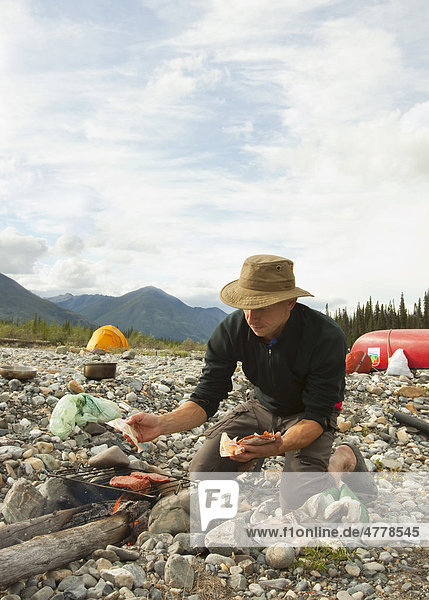 Mann kocht auf einem Lagerfeuer  grillt Hamburger  Kiesbank  Zelt  Camping  Wind River  Yukon Territory  Kanada