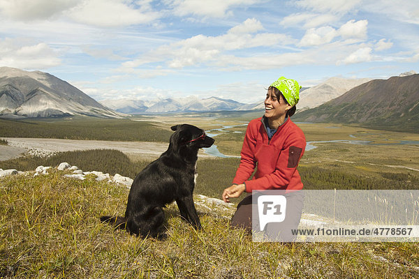 Junge Frau spielt mit ihrem Hund  Alaskan Husky  Schlittenhund  Aussicht  Wind River Tal und Mackenzie Mountains hinter  Yukon Territory  Kanada