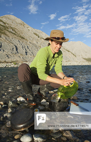 Young woman washing dishes in a river  camping  Mackenzie Mountains behind  Wind River  Yukon Territory  Canada
