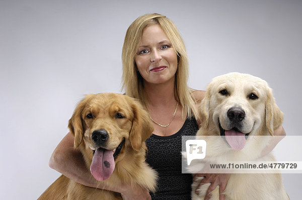 Frau umarmt zwei einjährige Golden Retriever