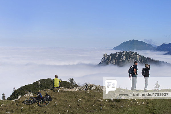 Hikers and a mountain biker looking onto the fog-shrouded Chiemgau Alps  Kampenwand mountain massif  Chiemgau  Upper Bavaria  Germany  Europe