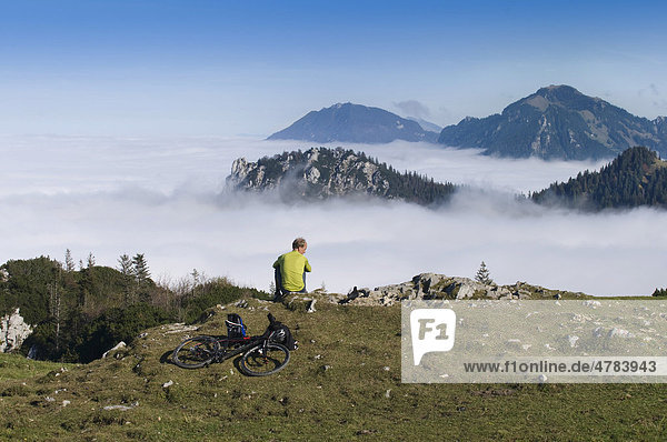 Kampenwand mountain massif  mountain biker resting on the mountain top overlooking the fog-shrouded Chiemgau Alps  Upper Bavaria  Germany  Europe