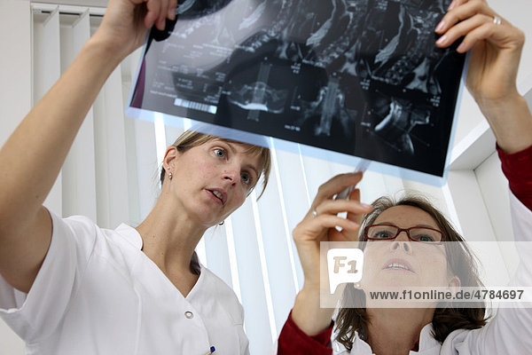 Arztpraxis  Ärztin schaut MRT-Bilder durch  Besprechung mit einer Praxismitarbeiterin