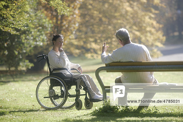 Frau sitzt im Rollstuhl  Mann sitzt auf Parkbank