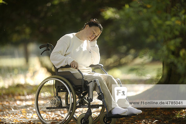 Frau sitzt mit geschlossenen Augen im Rollstuhl