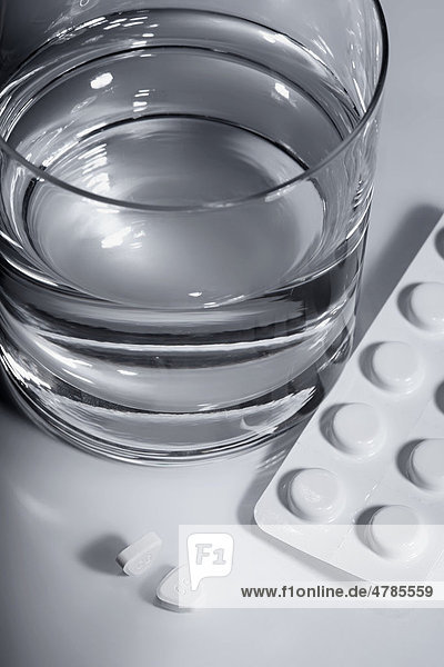 Tabletten liegen neben einem Wasserglas