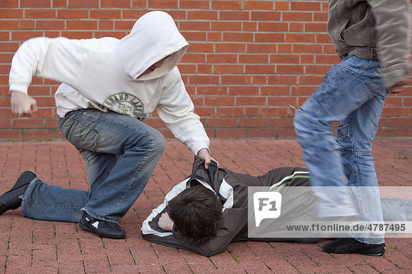 A defenseless boy lying on the ground while being held  kicked and beaten by two others  posed scene