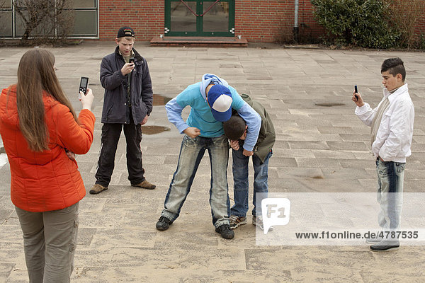 Two fighting boys are being filmed by three other teenagers with their mobile phone  reenactment