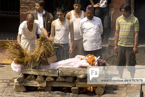 Teilnehmer eines traditionellen Begräbnis umstehen zur Verbrennung aufgebahrte Leiche eines Verwandten  während unberührbarer Priester der niedrigsten Kaste nasses Schilf über Leichnam breitet  Pashupatinath  Nepal  Asien