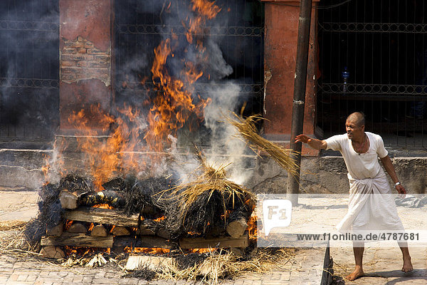 Unberührbarer Priester aus der untersten Kaste hält Scheiterhaufen bei traditioneller Leichenverbrennung am Brennen  Pashupatinath  Nepal  Asien