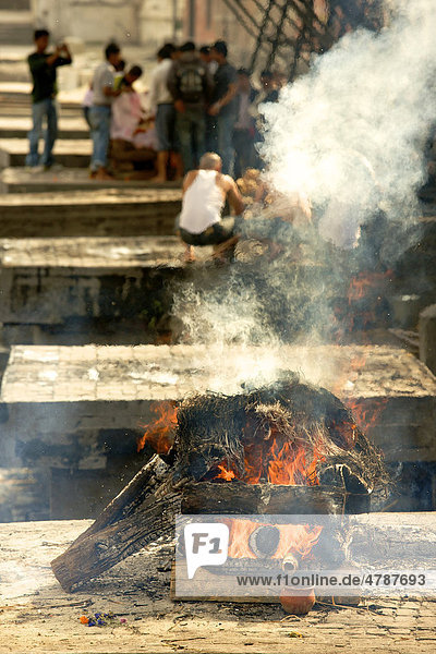 Brennender Scheiterhaufen am traditionellen Ort für Leichenverbrennung am heiligen Fluss Bagmati mit weiteren Plattformen mit Menschen dahinter  Pashupatinath  Nepal  Asien