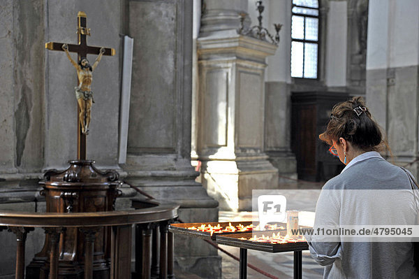 Woman in prayer with candles in front of Jesus on the cross in the nave of the Church of Santa Maria della Salute  Venezia  Venice  Italy  Europe
