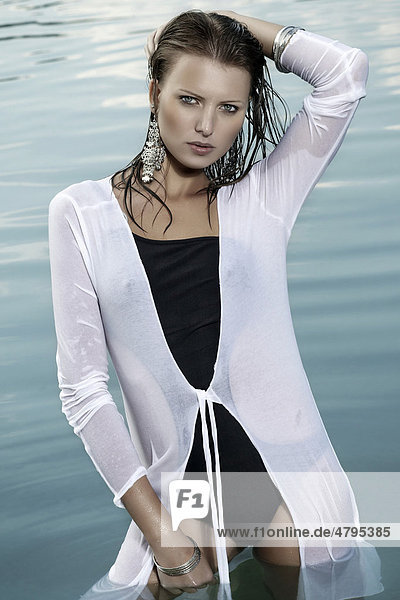 Junge Frau in einem schwarzen Badeanzug und weißem Oberteil und mit nassen Haaren beim Baden in einem See