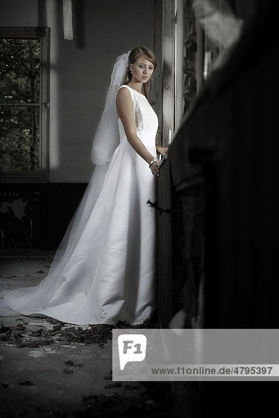 Junge Frau in einem Hochzeitskleid und Schleier steht in einer urbanen Location am Fenster