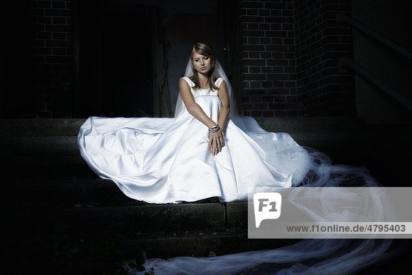 Junge Frau in einem Hochzeitskleid und Schleier sitzt in einer urbanen Location auf einer Treppe