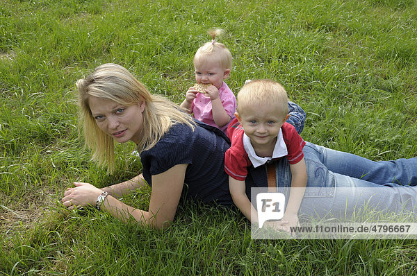 Young woman lying on grass with a girl  2 years  and a boy  4 years