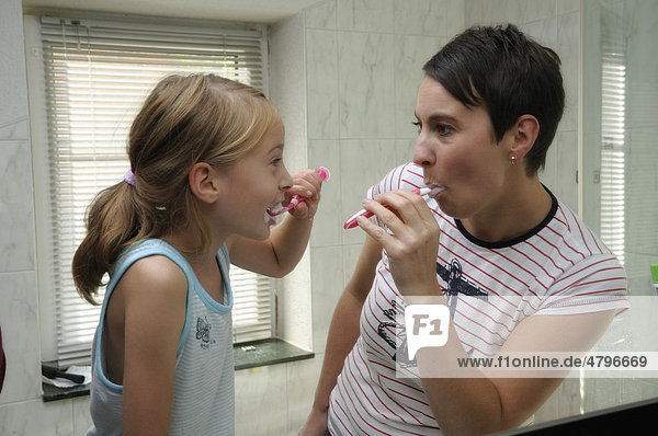 Woman  35 years  and girl  9 years  brushing their teeth