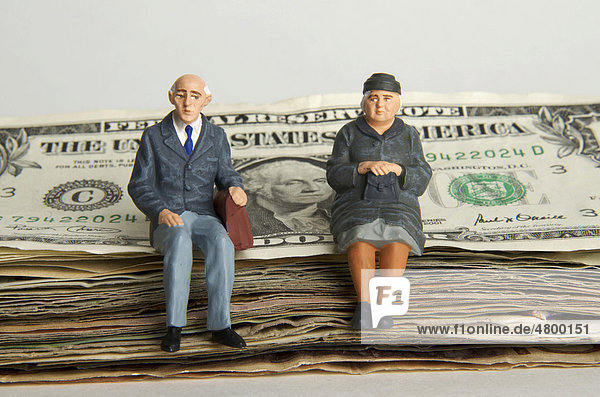 Älteres Paar  Figuren  sitzt auf einem Stapel Dollarscheine  Symbolbild Erbschaft