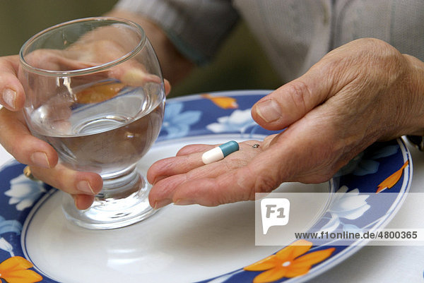 Hands of an elderly woman holding a pill and a glass of water