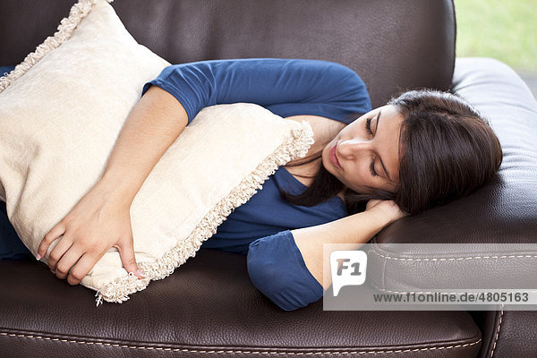 Junge Frau liegt auf einem Ledersofa und schläft mit Kissen im Arm