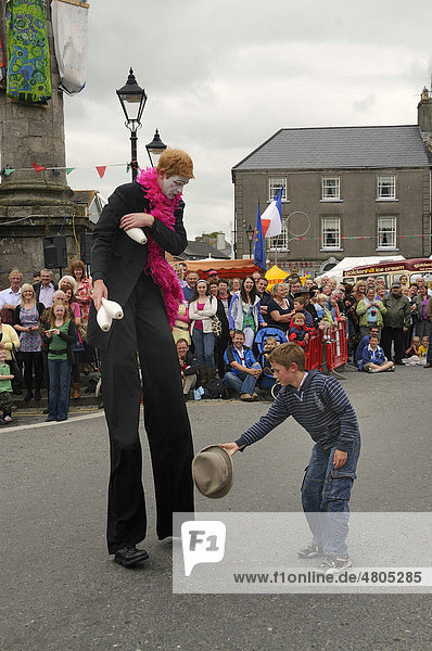 Stelzenmann lässt sich den heruntergefallenen Hut von einem Kind anreichen bei einem Umzug auf dem Stadtfest von Birr County Offaly Midlands Republik Irland Europa