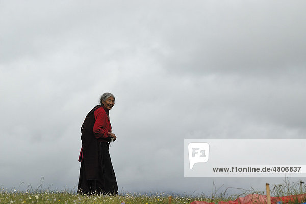 Elderly Tibetan woman wearing a traditional Tibetan costume  walking on a Kora pilgrimage in the grasslands of Tagong near the snow-covered peak of Mount Zhara Lhatse  5820 metres above sea level  Lhagang Monastery  Lhagang Gompa  Tagong  Sichuan province  China  Asia