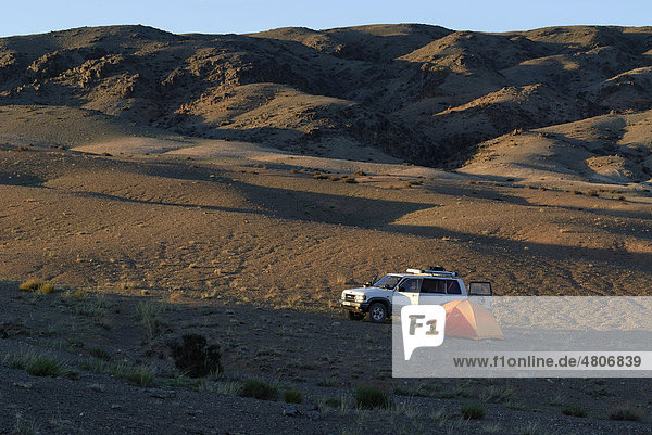 Weißer Opel Landcruiser steht im letzten Abendlicht neben Zeltlager mit Trekkingzelt und Outdoor Equipment in der Wüste Gobi  Khorgoryn Els  Gurvan Saikhan Nationalpark  Ömnögov Aimak  Mongolei  Asien