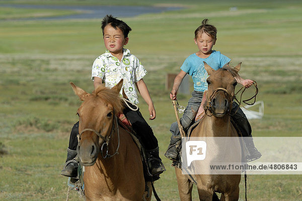 Zwei kleine 6jährige mongolische Jungen reiten im trockenen Grasland temperamentvolle mongolische Pferde ein  Lun  Töv Aimak  Mongolei  Asien