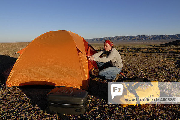 Junge Frau baut Zeltlager mit orangenem Trekkingzelt und Outdoor Equipment in der Wüste Gobi auf  Khorgoryn Els  Gurvan Saikhan Nationalpark  Ömnögov Aimak  Mongolei  Asien