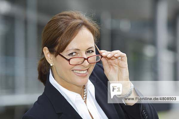 Geschäftsfrau  45 Jahre  im Kostüm  schaut lachend über den Brillenrand