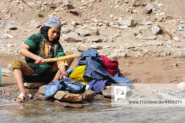 Junge Frau mit Kopftuch wäscht mit einem Waschknüppel Wäsche am Flussufer  Hoher Atlas  Marokko  Afrika