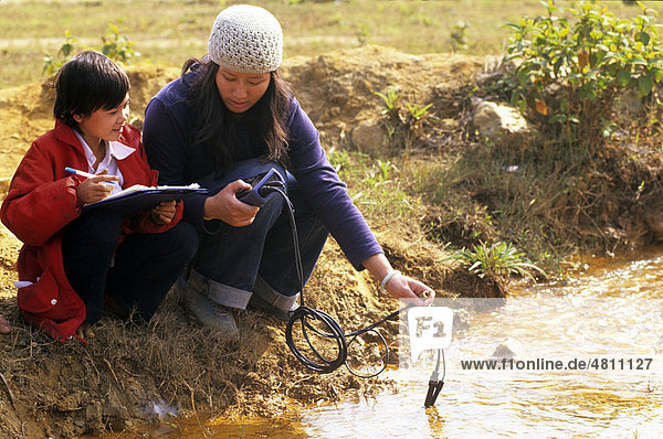 Ein einheimisches Kind hilft einem Umweltberater beim Prüfen der Wasserqualität an einem Fluss in der Nähe einer Mine  Metall-Oxidation  Provinz Thai Nguyen  Vietnam  Südostasien  Asien