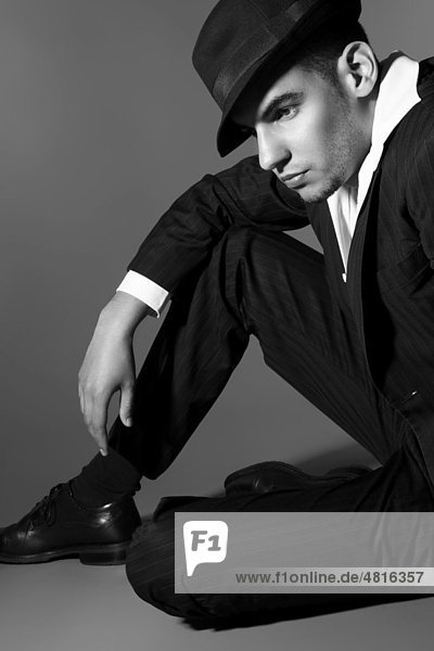 Young man in suit  shirt  tie and hat  sitting on the ground lost in thought