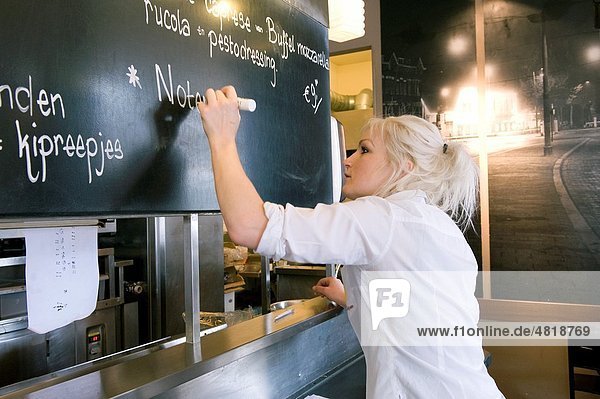 A young waitress is writing the menu of the day to the blackboard of a restaurant