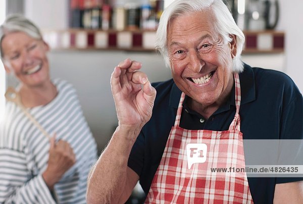 Senior man gesturing  woman cooking in background