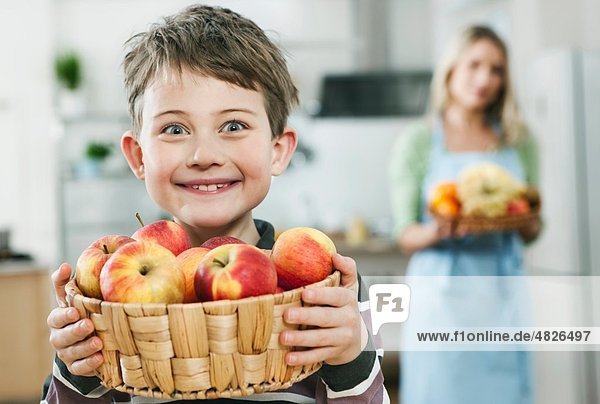 Junge hält Apfelkorb mit Mutter im Hintergrund