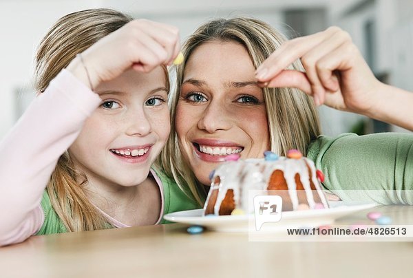 Deutschland    Mutter und Tochter schmücken Kuchen  lächelnd  Portrait