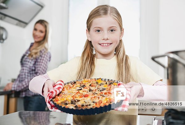 Girl holding pizza with mother in background