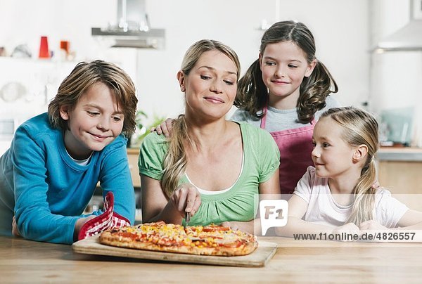 Deutschland    Mutter und Kinder schauen sich Pizza an und lächeln