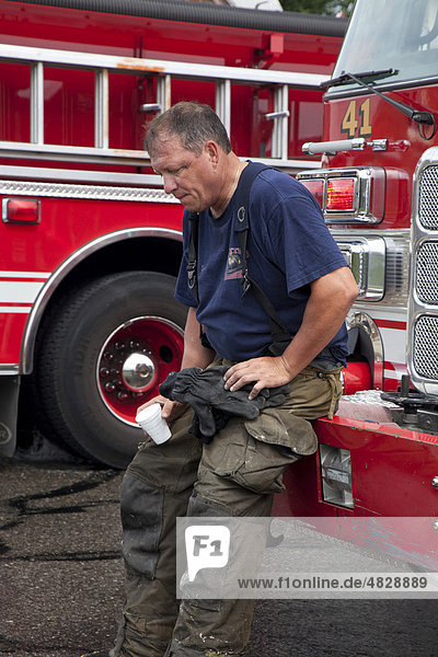 An exhausted fire fighter takes a break while battling a house fire in hot summer weather  Detroit  Michigan  USA
