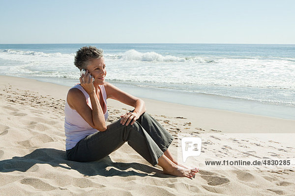Senior woman using cell phone on beach