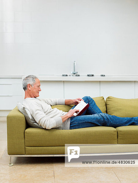 Senior man sitting on sofa reading book