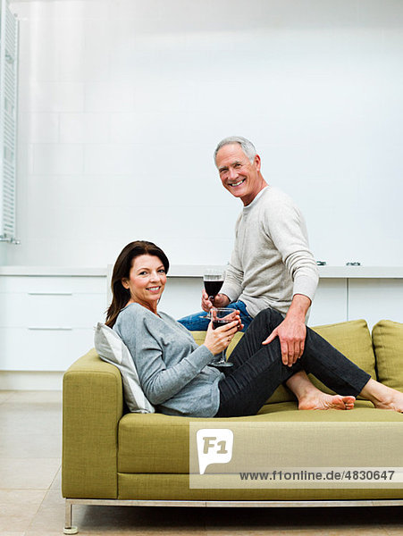 Erwachsenes Paar auf dem Sofa sitzend mit Wein