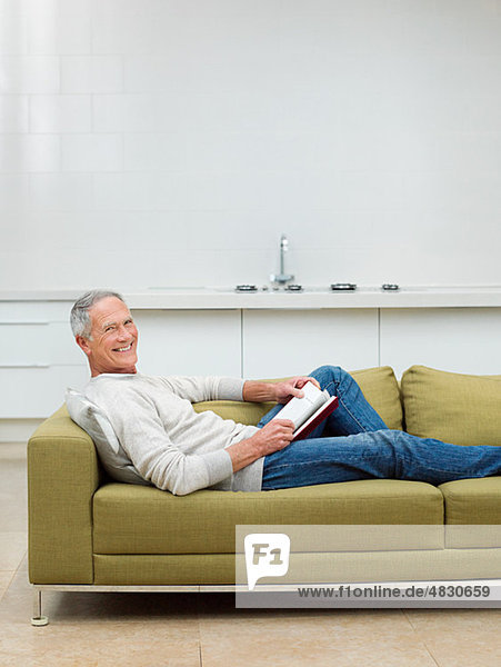Senior man sitting on sofa reading book