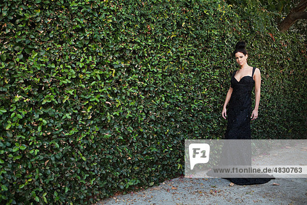 Junge Frau tragen schwarz Abendkleid  einstehen hedge