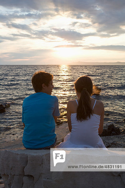 Teenage couple watching sunset over sea